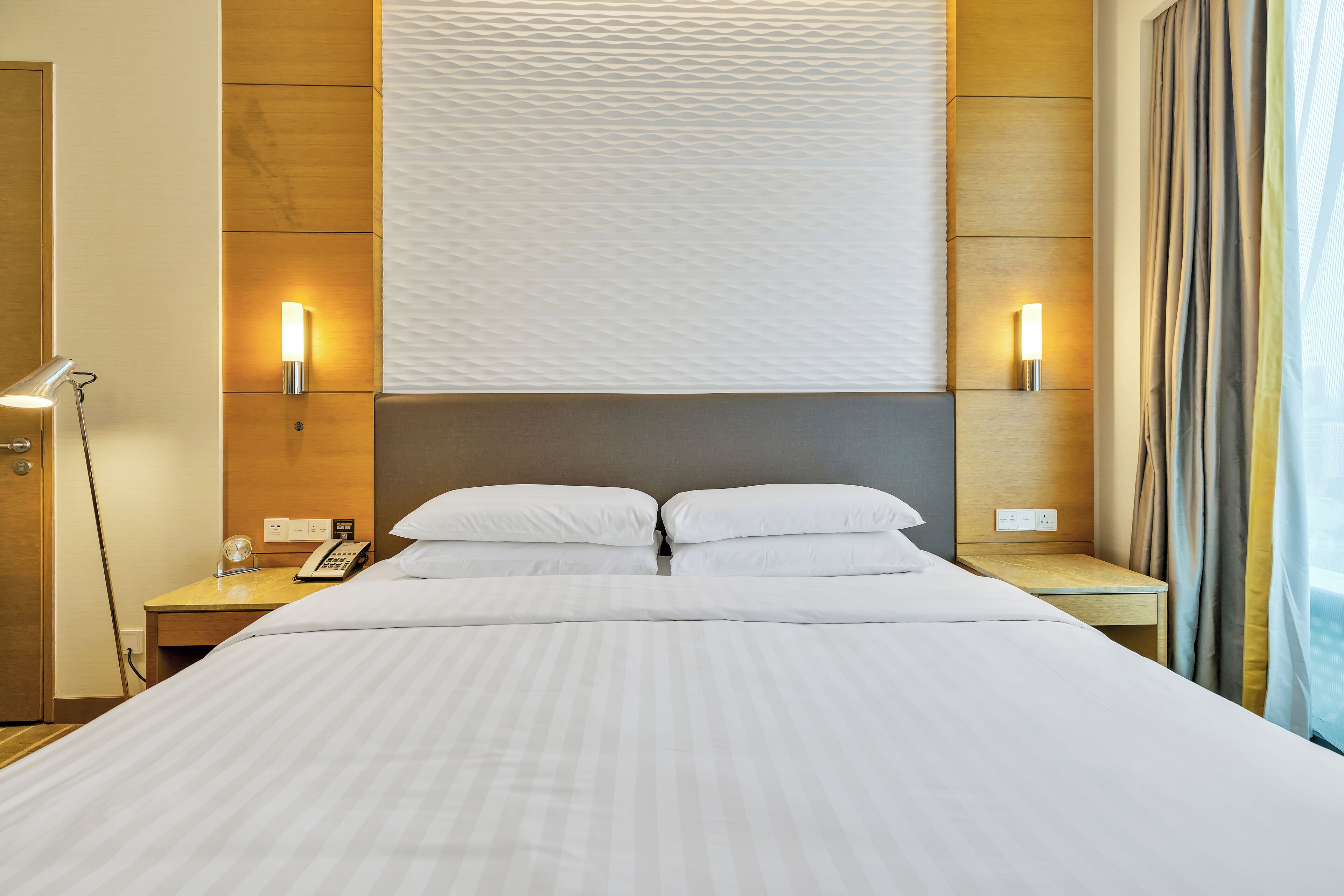 A hotel room with a large bed, two bedside tables, a desk, a lamp, and a wall-mounted light fixture.