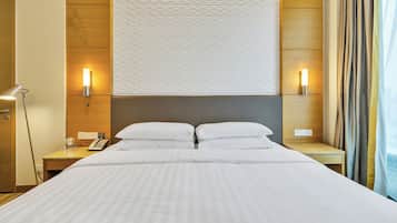 Habitación de hotel con una cama grande, dos mesitas de noche, un escritorio, una lámpara y un aplique de pared.