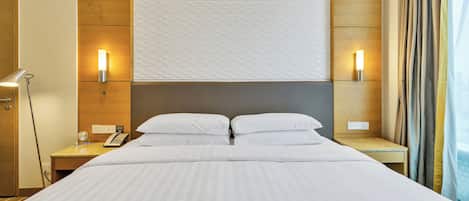 A hotel room with a large bed, two bedside tables, a desk, a lamp, and a wall-mounted light fixture.