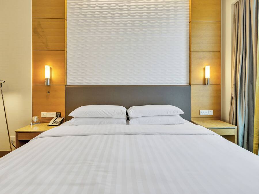 Habitación de hotel con una cama grande, dos mesitas de noche, un escritorio, una lámpara y un aplique de pared.