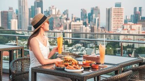 Una persona sta cenando a un tavolo all'aperto con lo skyline della città sullo sfondo.