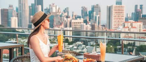 Una persona cenando en una mesa al aire libre con un horizonte urbano de fondo.