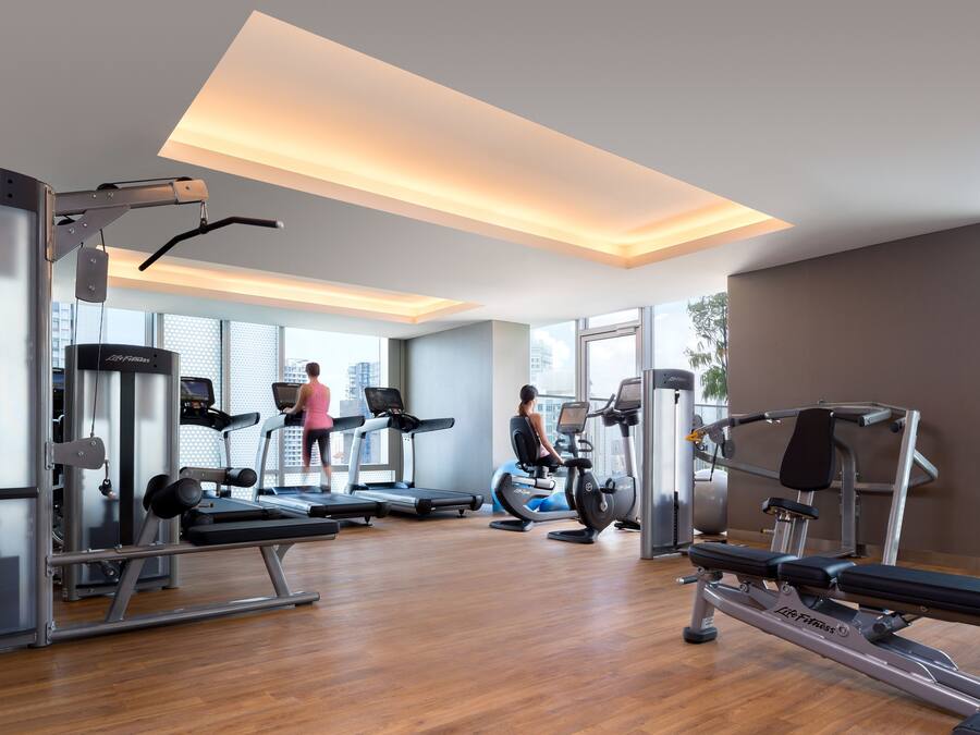 A modern gym with treadmills, weight machines, and a large window offering a city view.