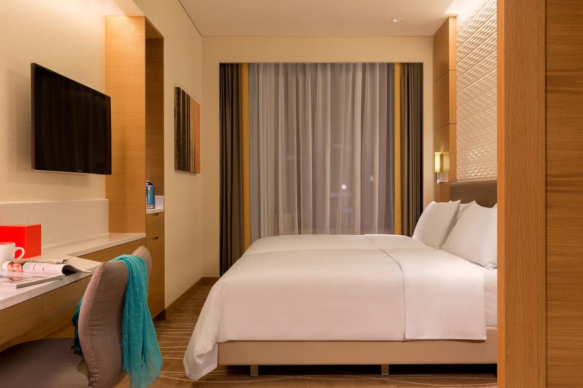 Una habitación de hotel con cama, escritorio, silla, televisor y ventana con cortinas.