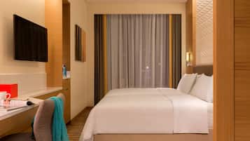 A hotel room with a bed, a desk, a chair, a TV, and a window with curtains.