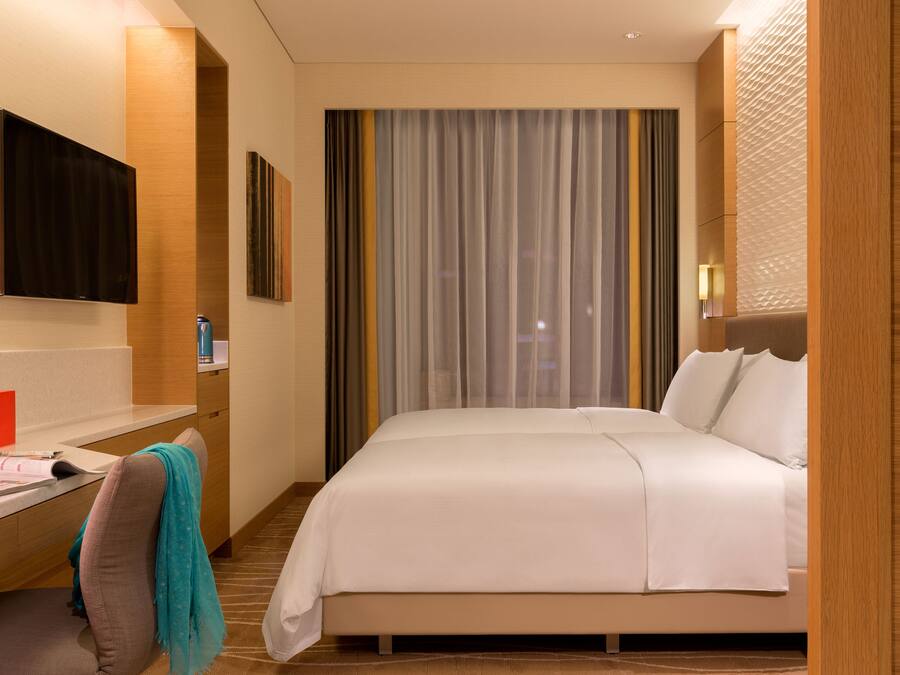 A hotel room with a bed, a desk, a chair, a TV, and a window with curtains.