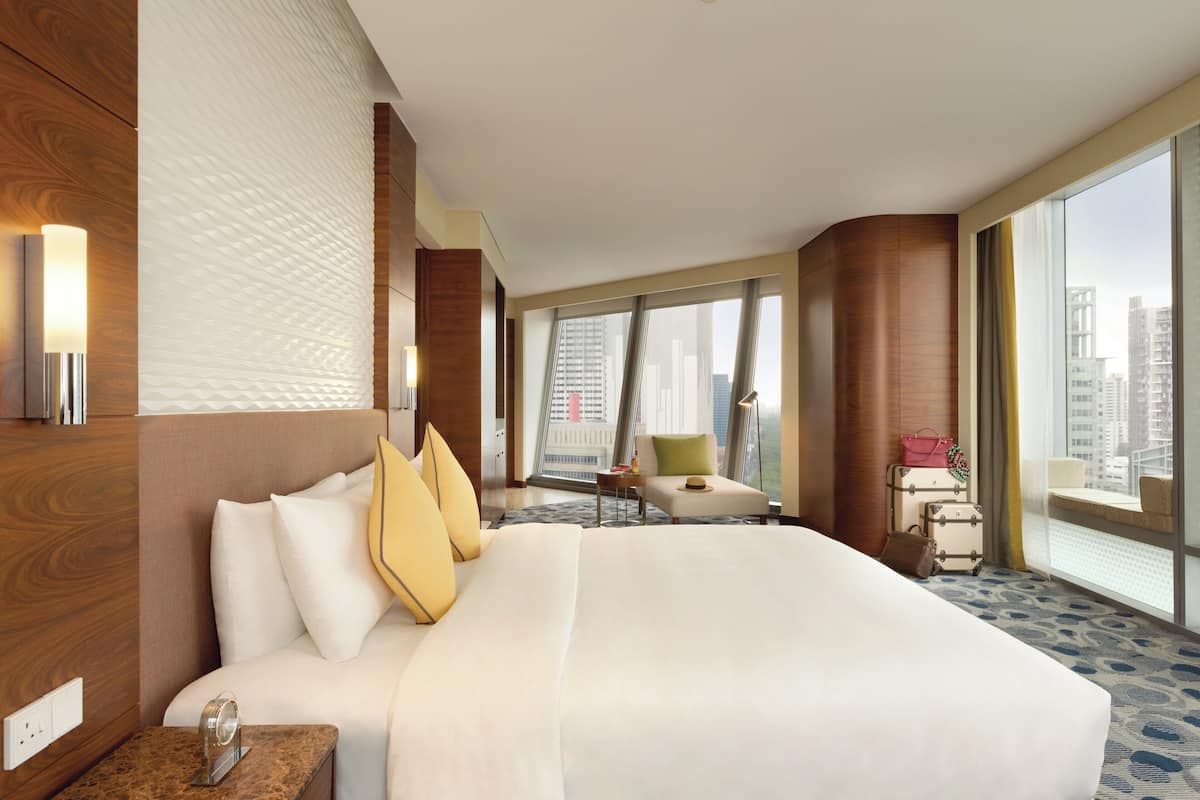 Habitación de hotel con una cama grande, zona de estar y vistas a la ciudad.