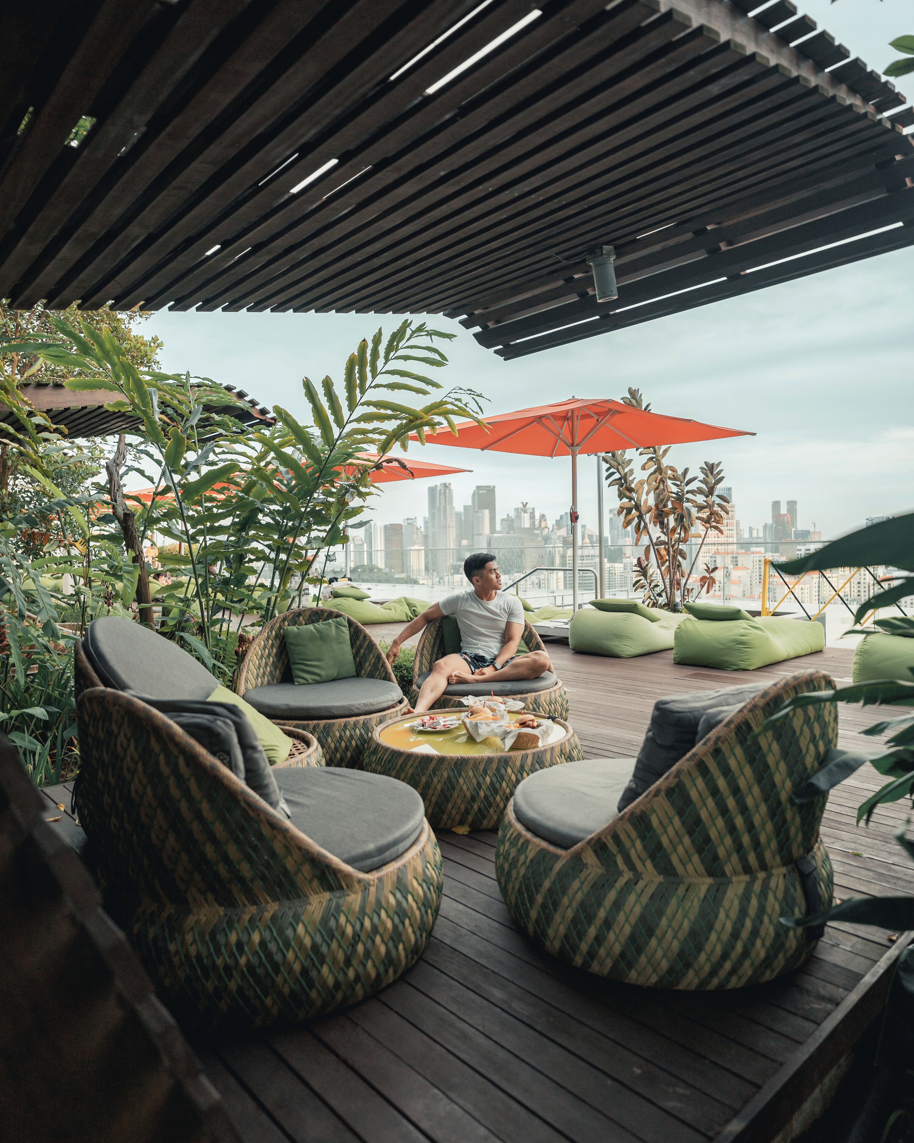 A rooftop terrace with wicker furniture, green cushions, and red umbrellas.