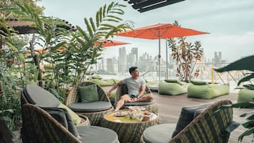 A rooftop terrace with wicker furniture, green cushions, and red umbrellas.