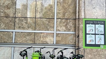 Une station de vélos en libre-service, avec des instructions sur la façon d’utiliser le service, située devant un immeuble doté de grandes fenêtres.
