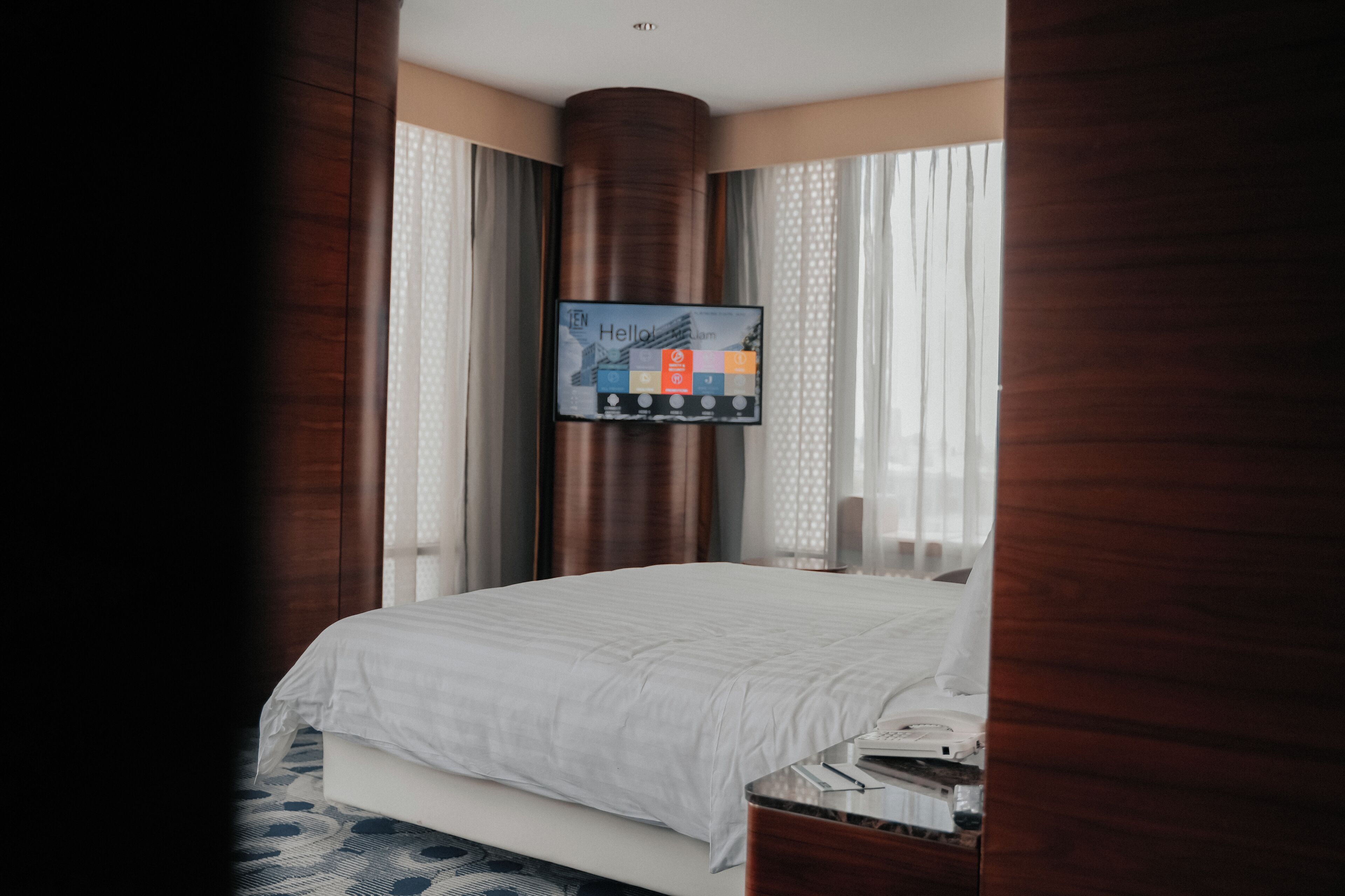 A hotel room with a bed, a television mounted on the wall, and a window with curtains.