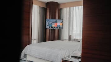 A hotel room with a bed, a television mounted on the wall, and a window with curtains.