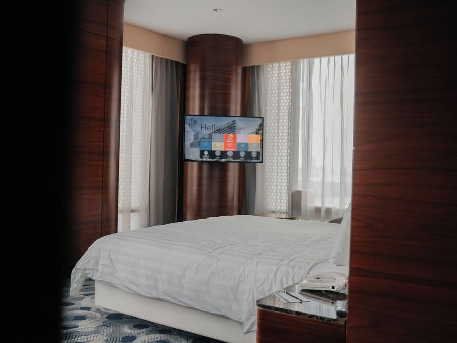 A hotel room with a bed, a television mounted on the wall, and a window with curtains.