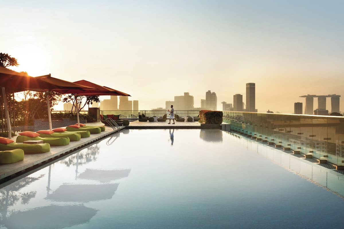 Piscina infinita en la azotea con vista al horizonte de la ciudad, asientos exteriores y sombrillas.