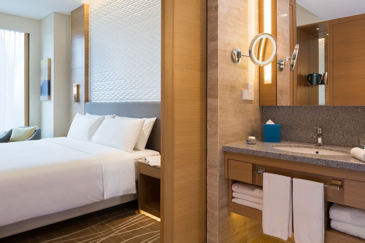 Una habitación de hotel con cama, baño con lavamanos, espejo y toallas.