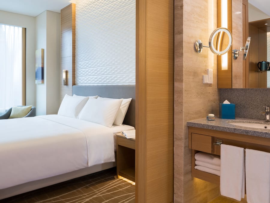 Una habitación de hotel con cama, baño con lavamanos, espejo y toallas.