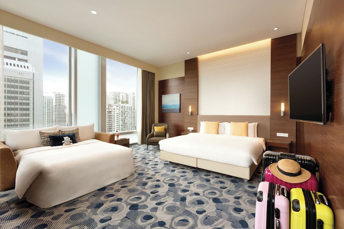 Habitación de hotel con dos camas, un ventanal con vista a la ciudad, un televisor de pantalla plana y un perchero para equipaje.