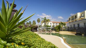 Un área de piscina con sillones de descanso y sombrillas, rodeada de vegetación y palmeras.