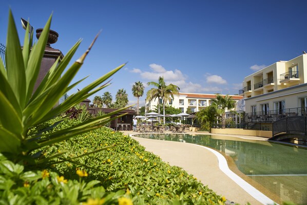 Un área de piscina con sillones de descanso y sombrillas, rodeada de vegetación y palmeras.