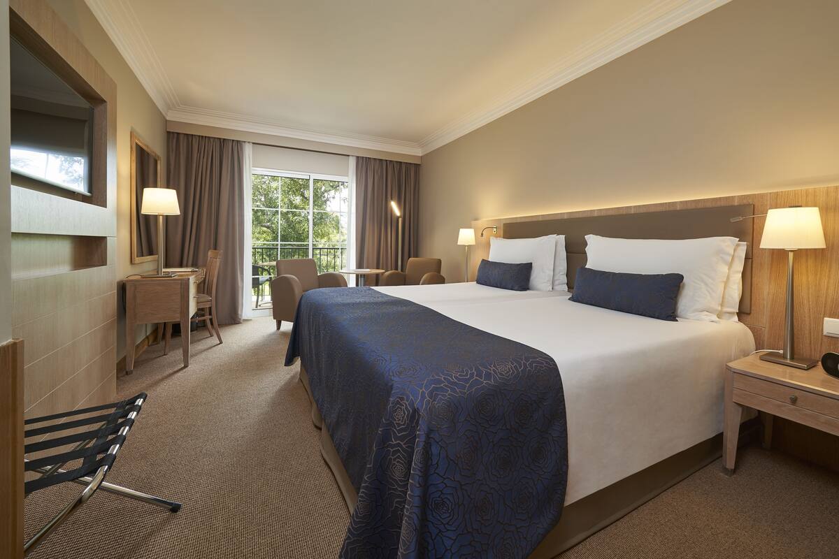 Ein Hotelzimmer mit einem großen Bett, zwei Nachttischen, einem Schreibtisch mit Stuhl, einer Couch und einem großen Fenster mit Vorhängen.