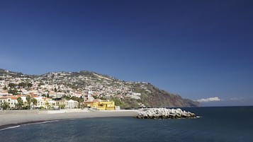 Un pueblo costero con un edificio amarillo destacado, un rompeolas rocoso y una colina con numerosas casas.