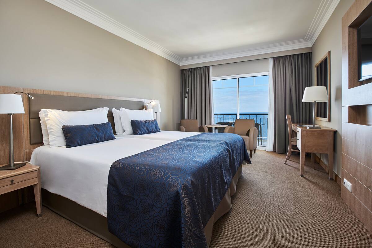 Ein Hotelzimmer mit einem großen Bett, einem Schreibtisch und Meerblick.