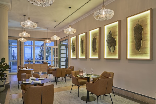 A modern dining area with pendant lighting, framed artwork, and a view of the outdoors. - PortoBay Santa Maria, Adults Only (Funchal)