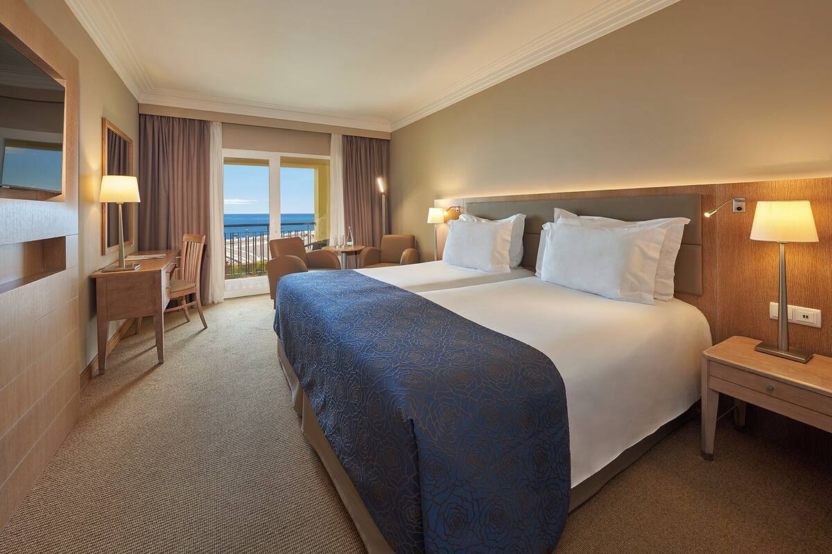 Ein Hotelzimmer mit einem großen Bett, einem Schreibtisch, einem Stuhl, einer Lampe und Blick auf den Ozean.