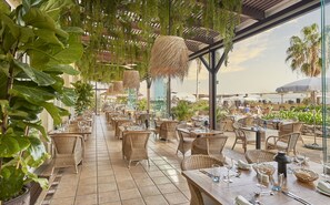 Un restaurant en plein air avec des meubles en osier, un sol carrelé et des plantes suspendues.