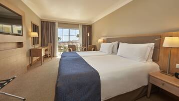A hotel room with two beds, a desk, chairs, and a balcony with a view.