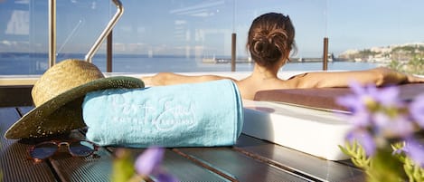 A person relaxing on a sun lounger with a view of the sea and a cityscape.