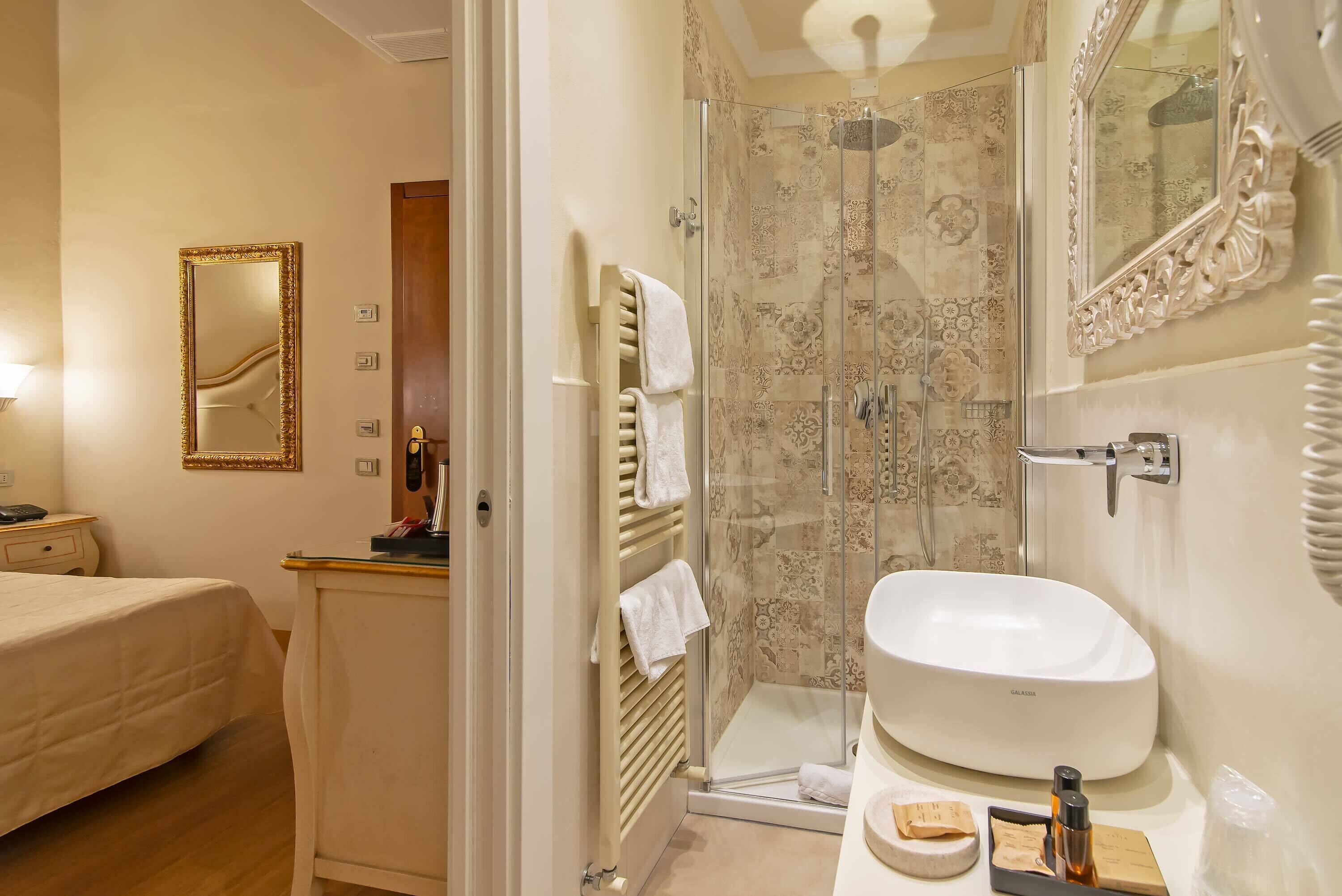 A hotel bathroom with a glass-enclosed shower, a white sink, and a large mirror.