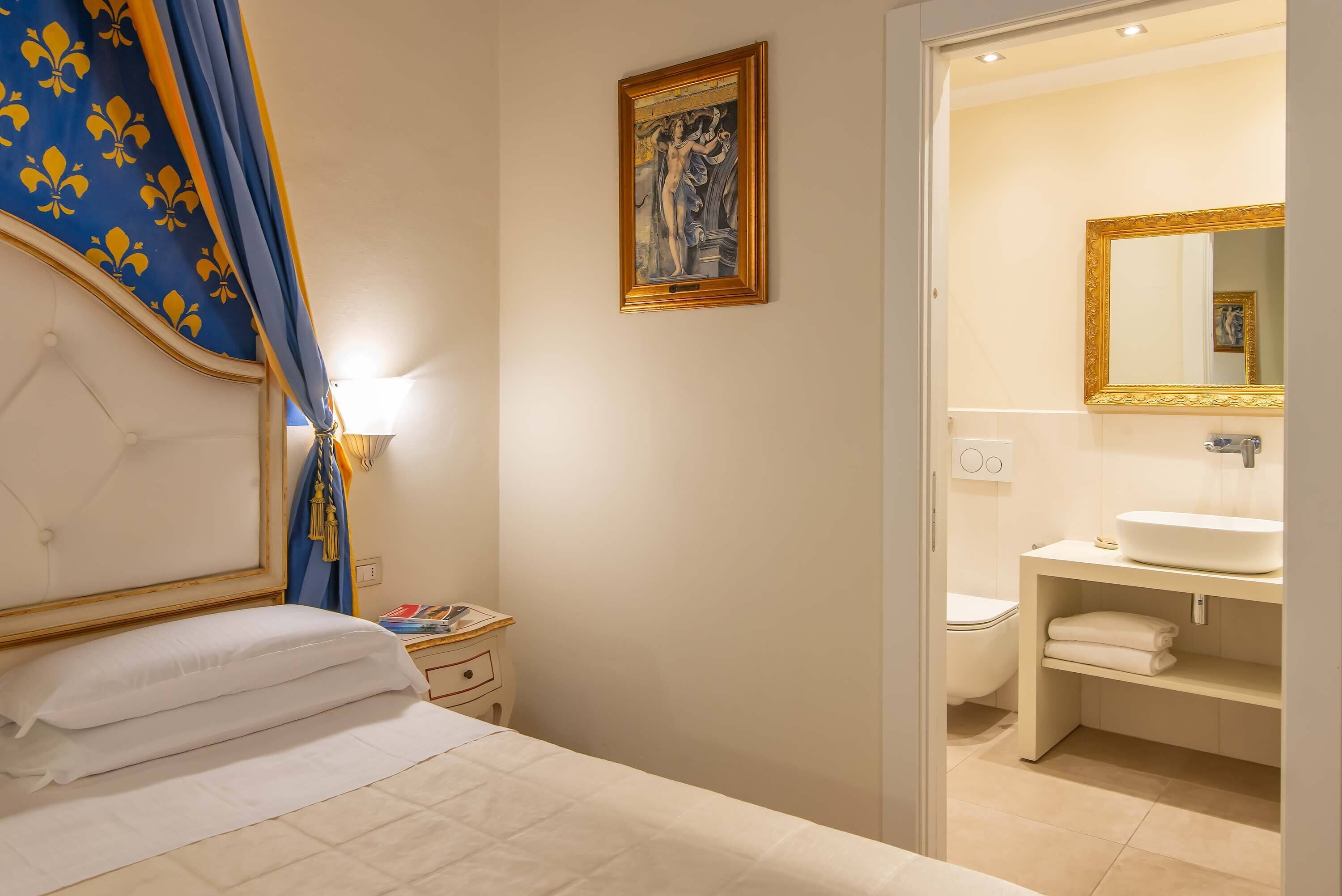 A hotel room with a bed, a nightstand, a framed artwork, a bathroom with a sink and mirror.