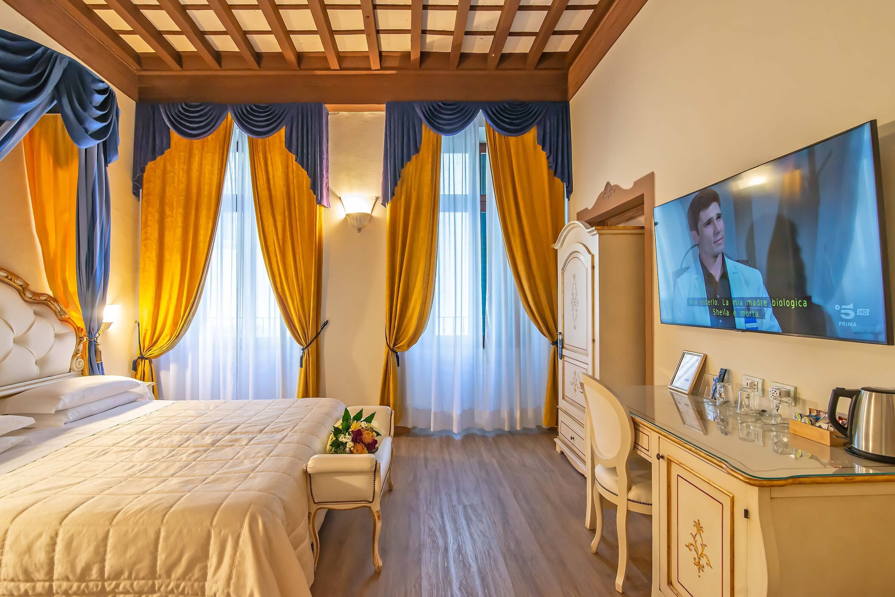 A hotel room with a large bed, a desk with a mirror, and a TV displaying a program.