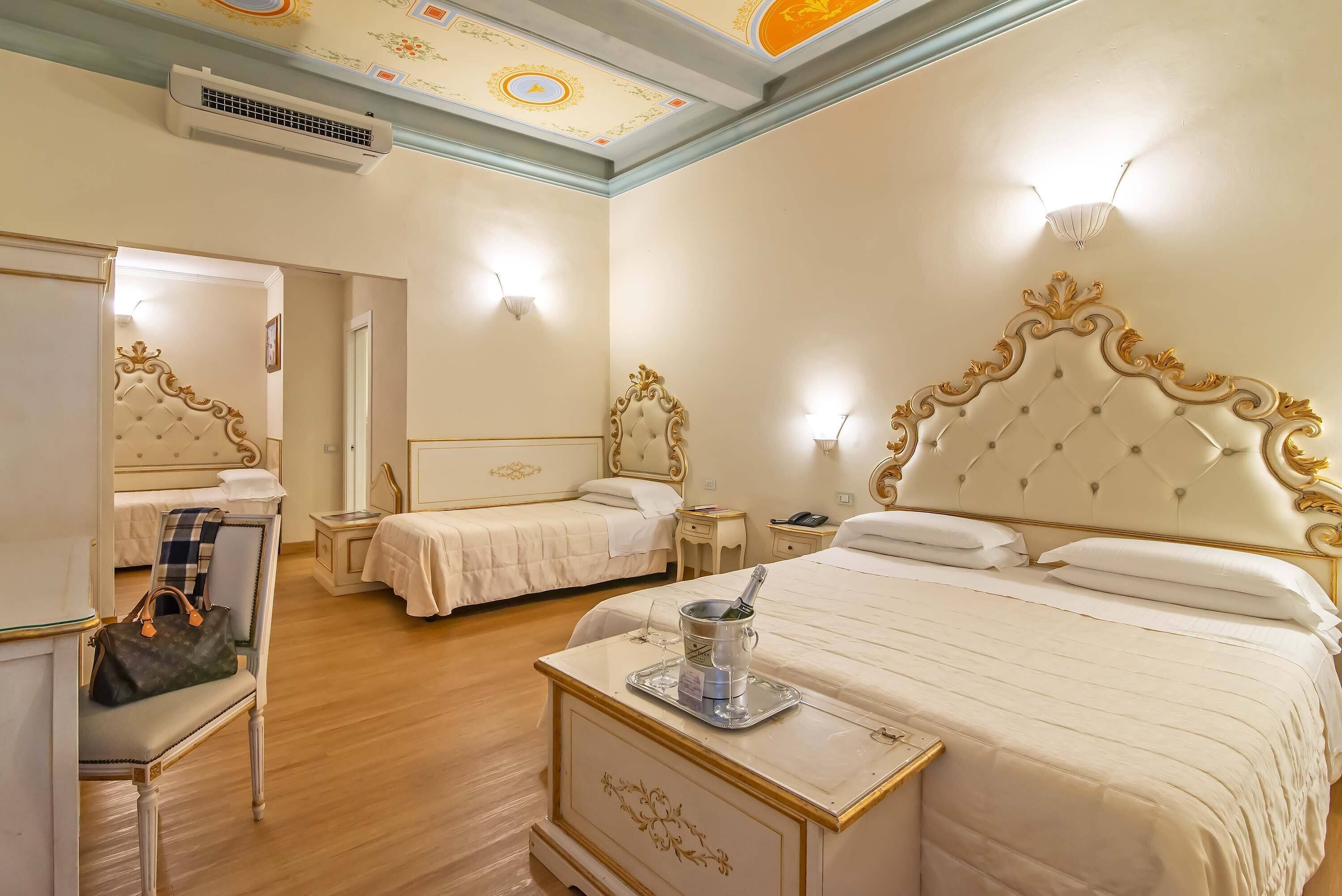 A hotel room with two beds, a vanity with a mirror, a small table with a bucket, and a wall-mounted air conditioner.