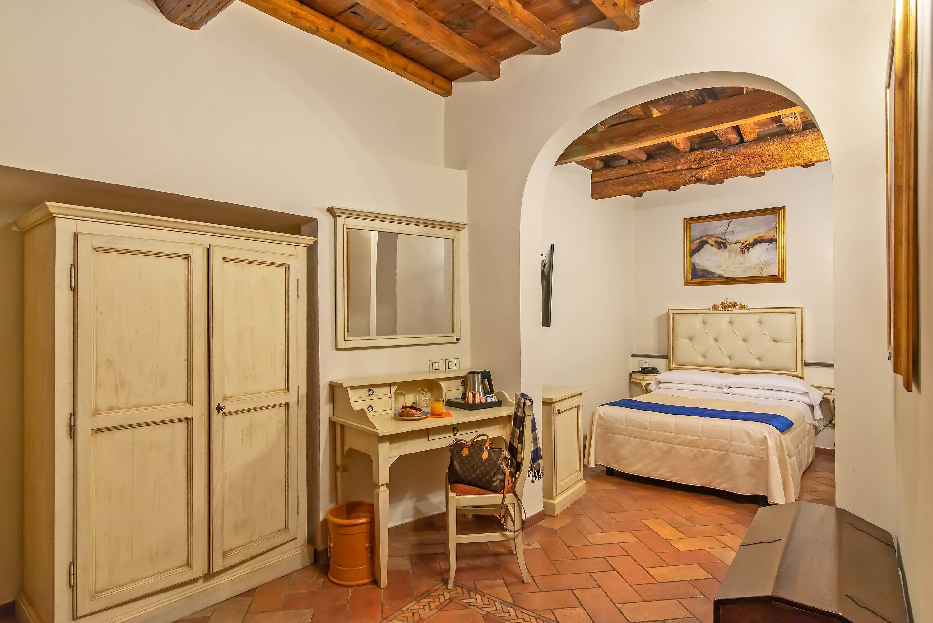 A bedroom with a bed, a desk, a chair, a wardrobe, and a painting on the wall.