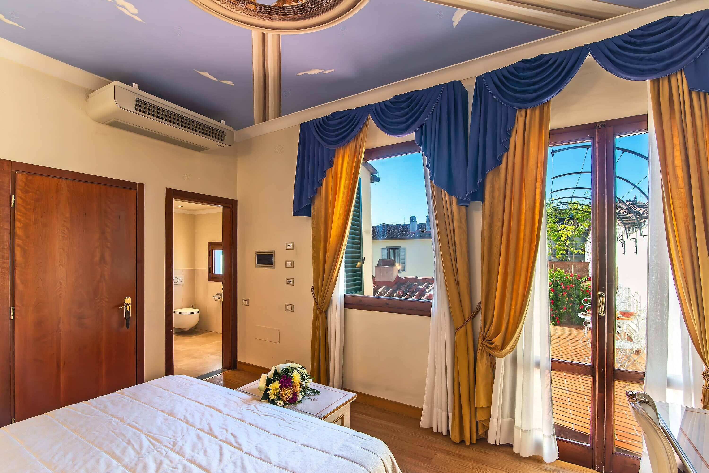A bedroom with a bed, a window with curtains, a door, and an air conditioning unit.