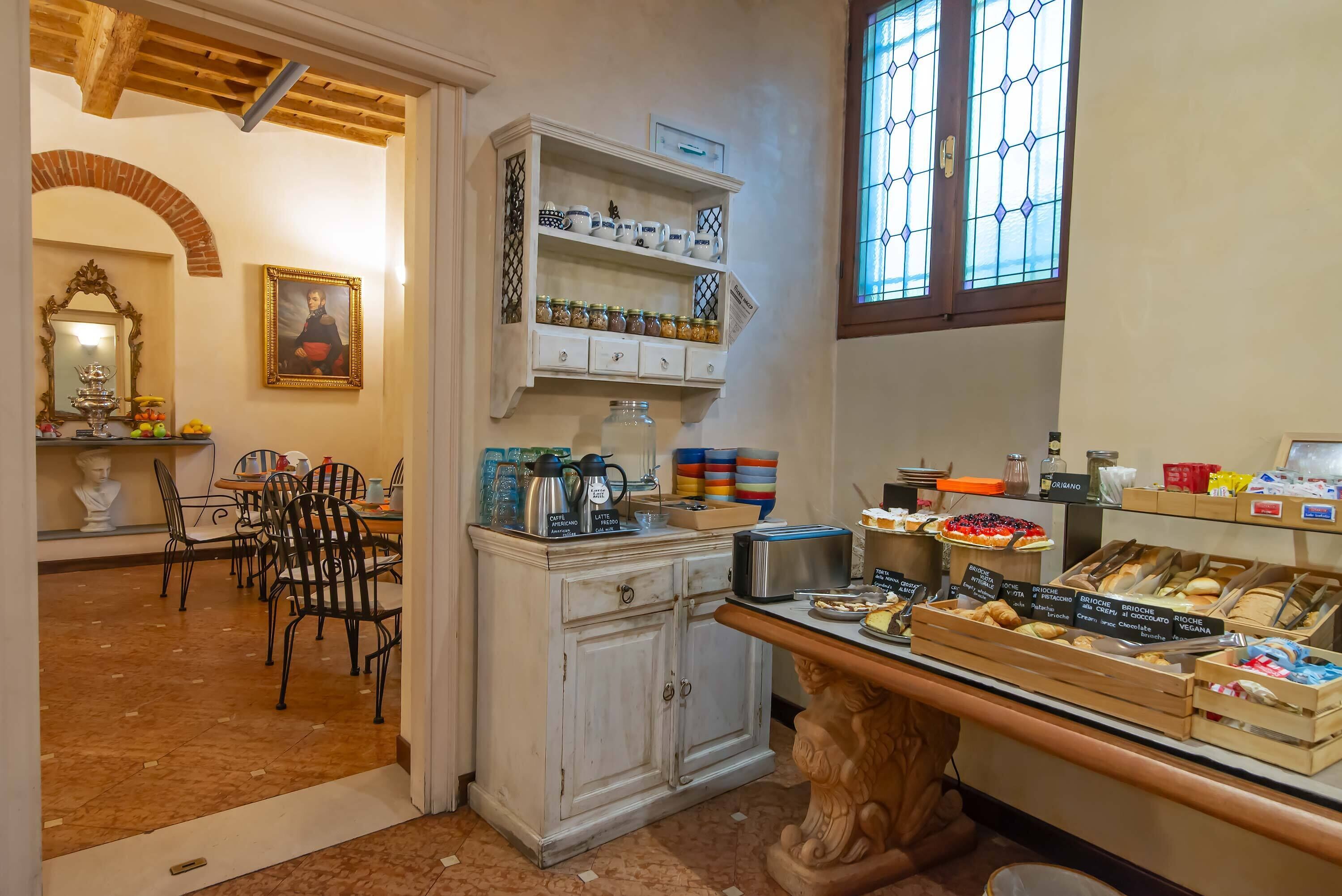 A dining area with a buffet setup, a white cabinet with shelves, and a window with stained glass.