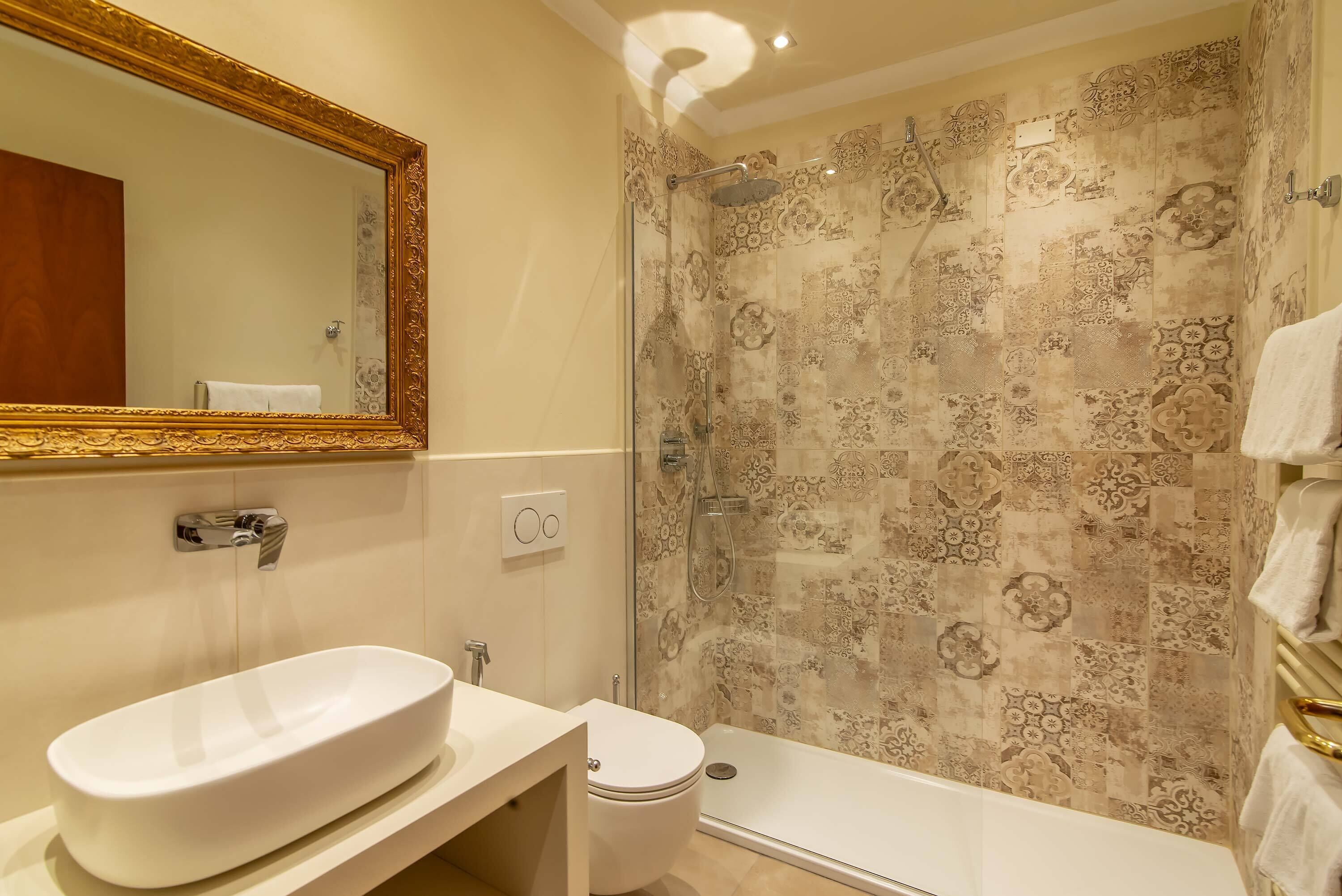 Une salle de bain avec un grand lavabo ovale, des toilettes et une douche aux carreaux décorés.