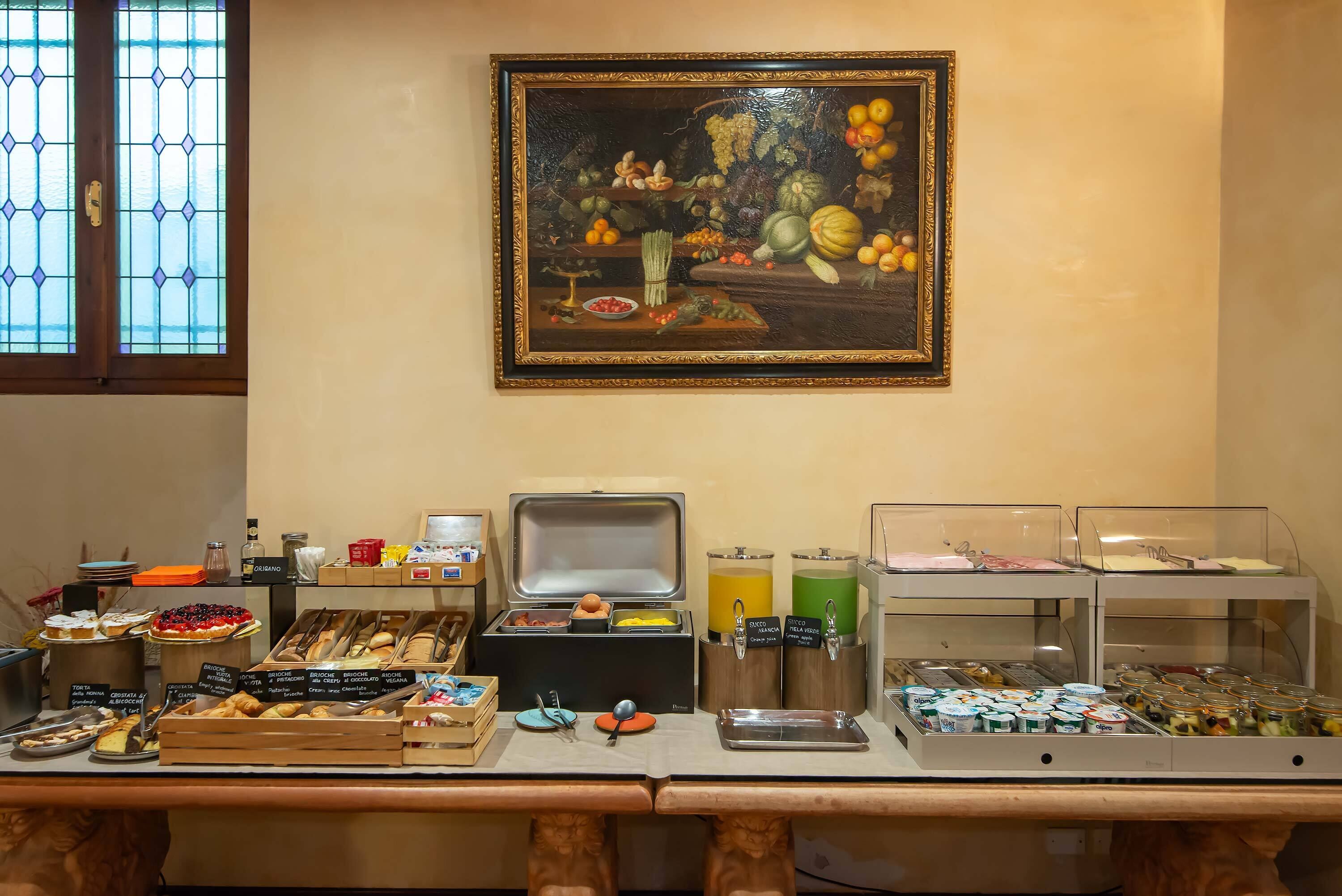 A breakfast buffet with various food items and a painting of fruits on the wall.