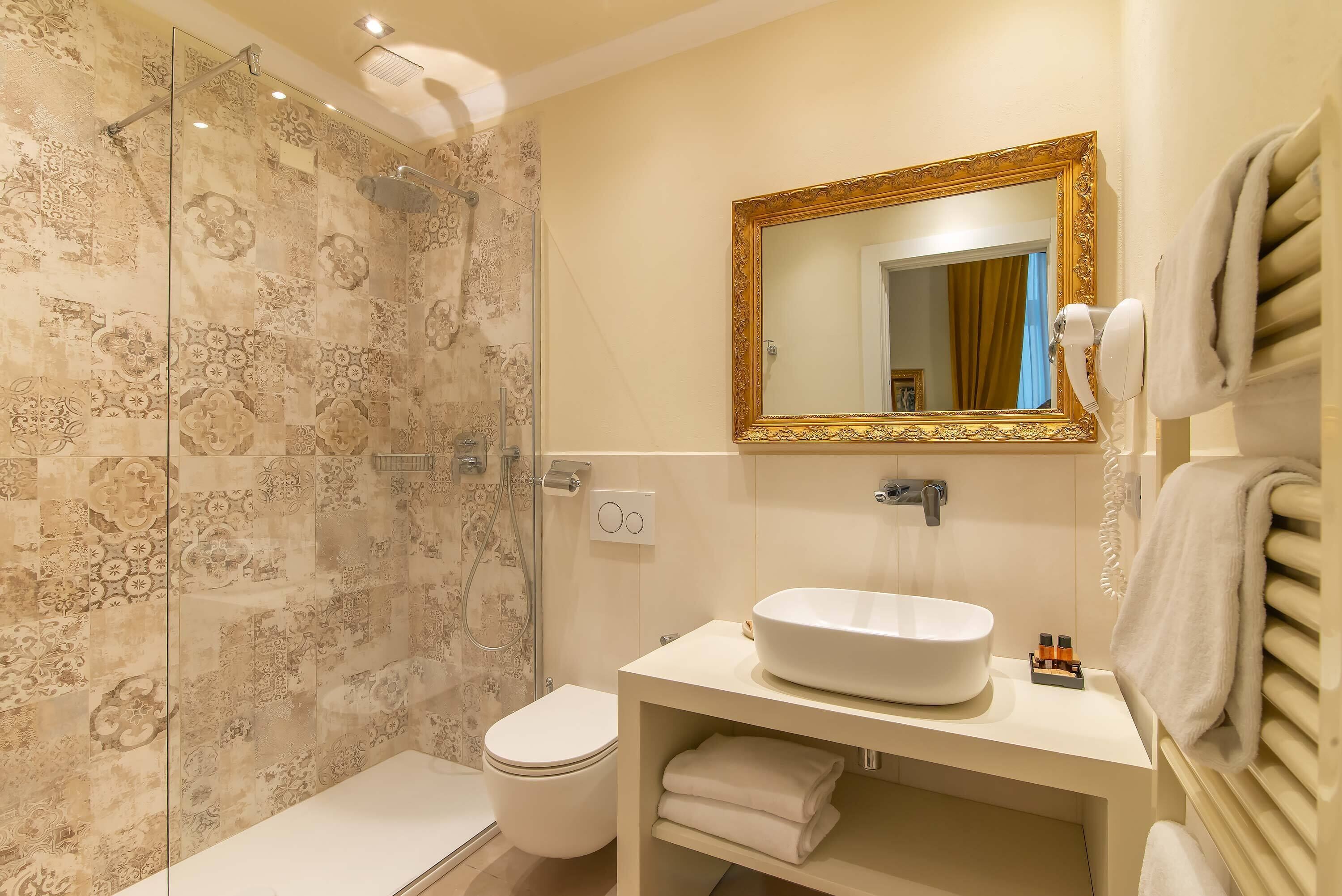 A bathroom with a shower, toilet, sink, and a mirror with a gold frame.