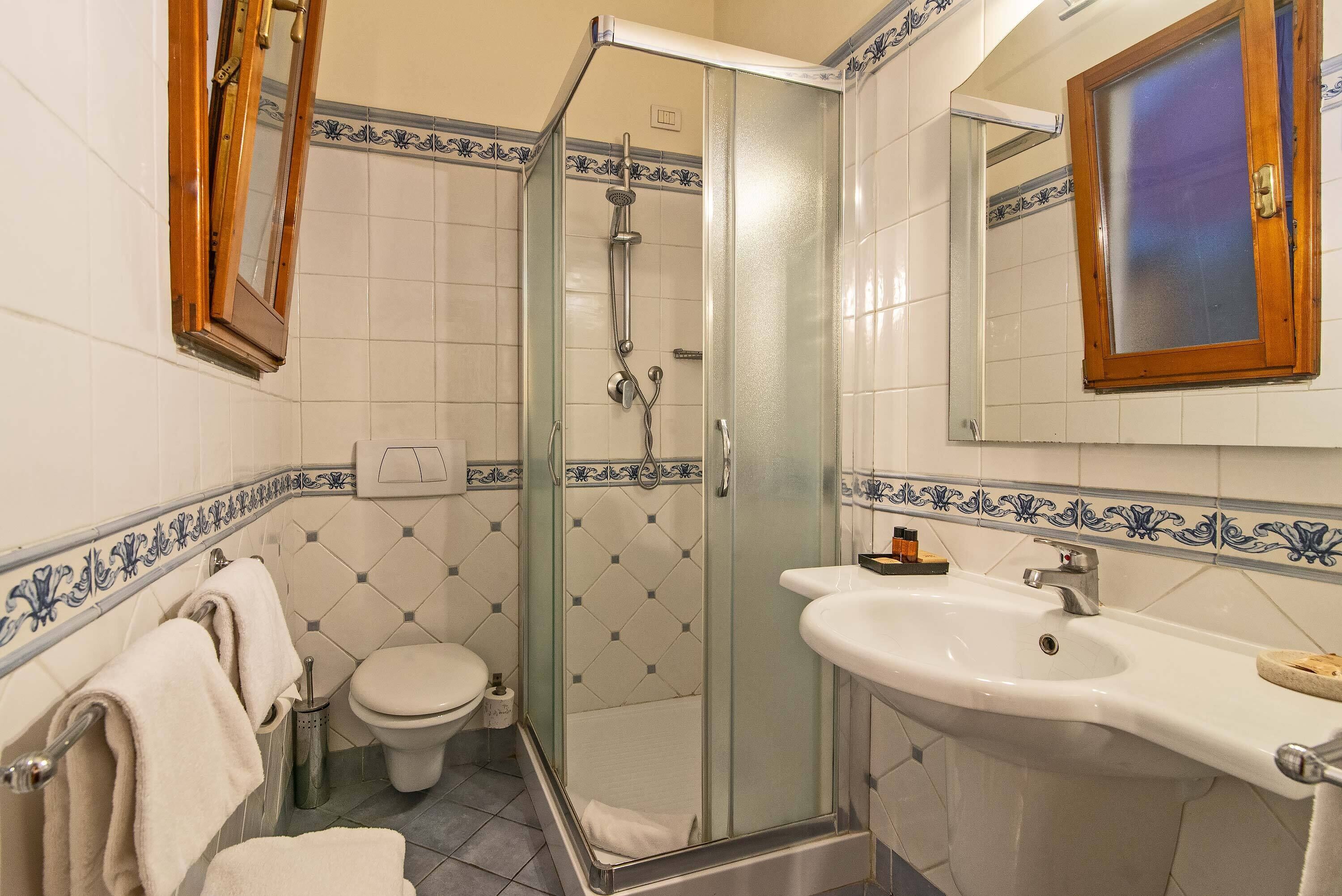 Un baño con ducha de vidrio, lavamanos blanco y retrete.