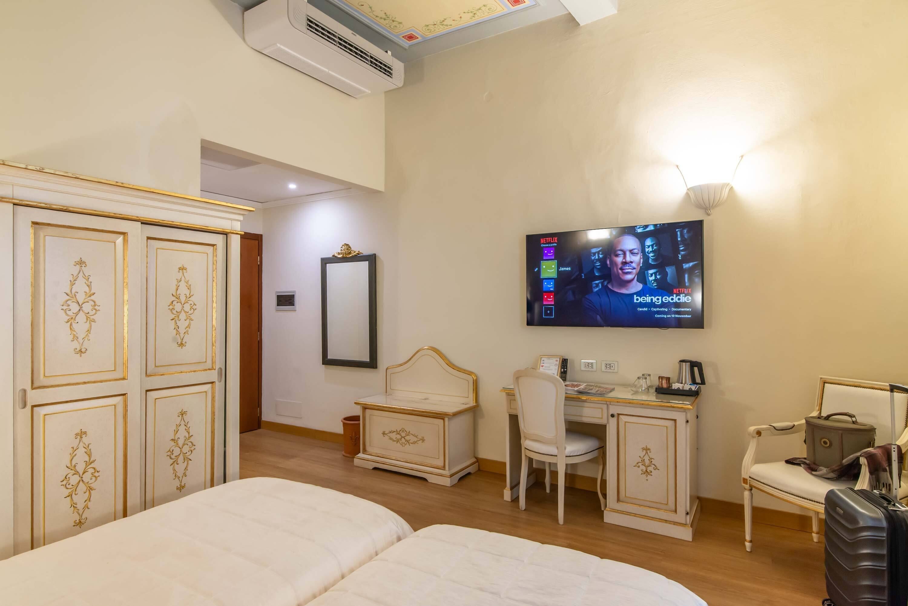 A hotel room with two beds, a desk with a chair, a television mounted on the wall, and a wardrobe with decorative panels.