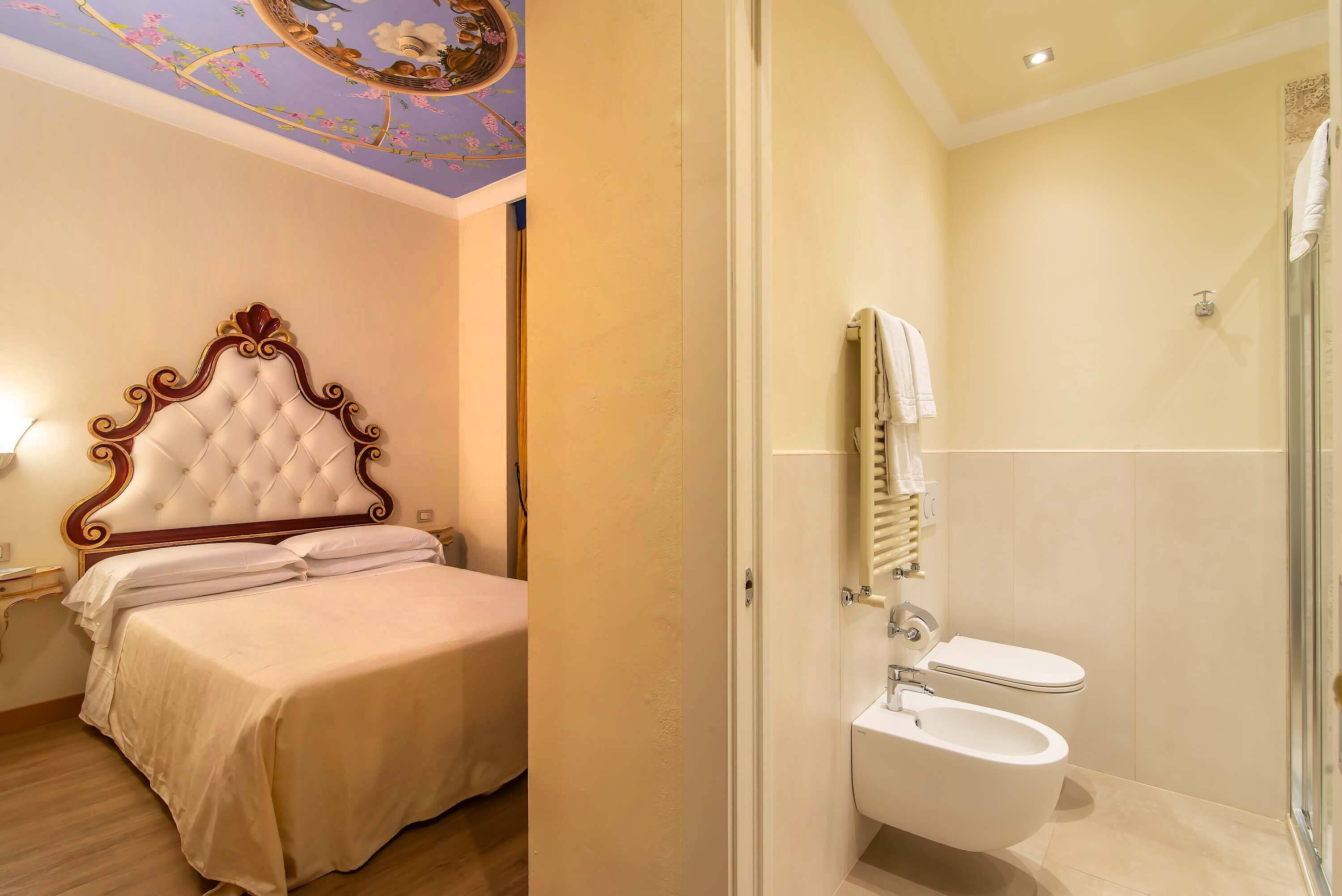 A bedroom with a large bed, a bathroom with a toilet and shower, and a ceiling with floral patterns.