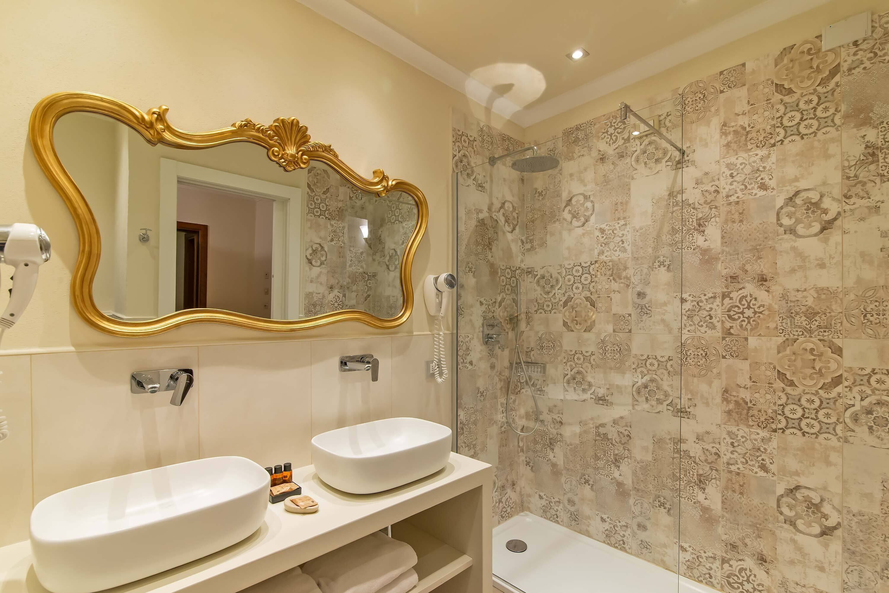 Een badkamer met twee wastafels, een grote spiegel en een douche met betegelde wanden.