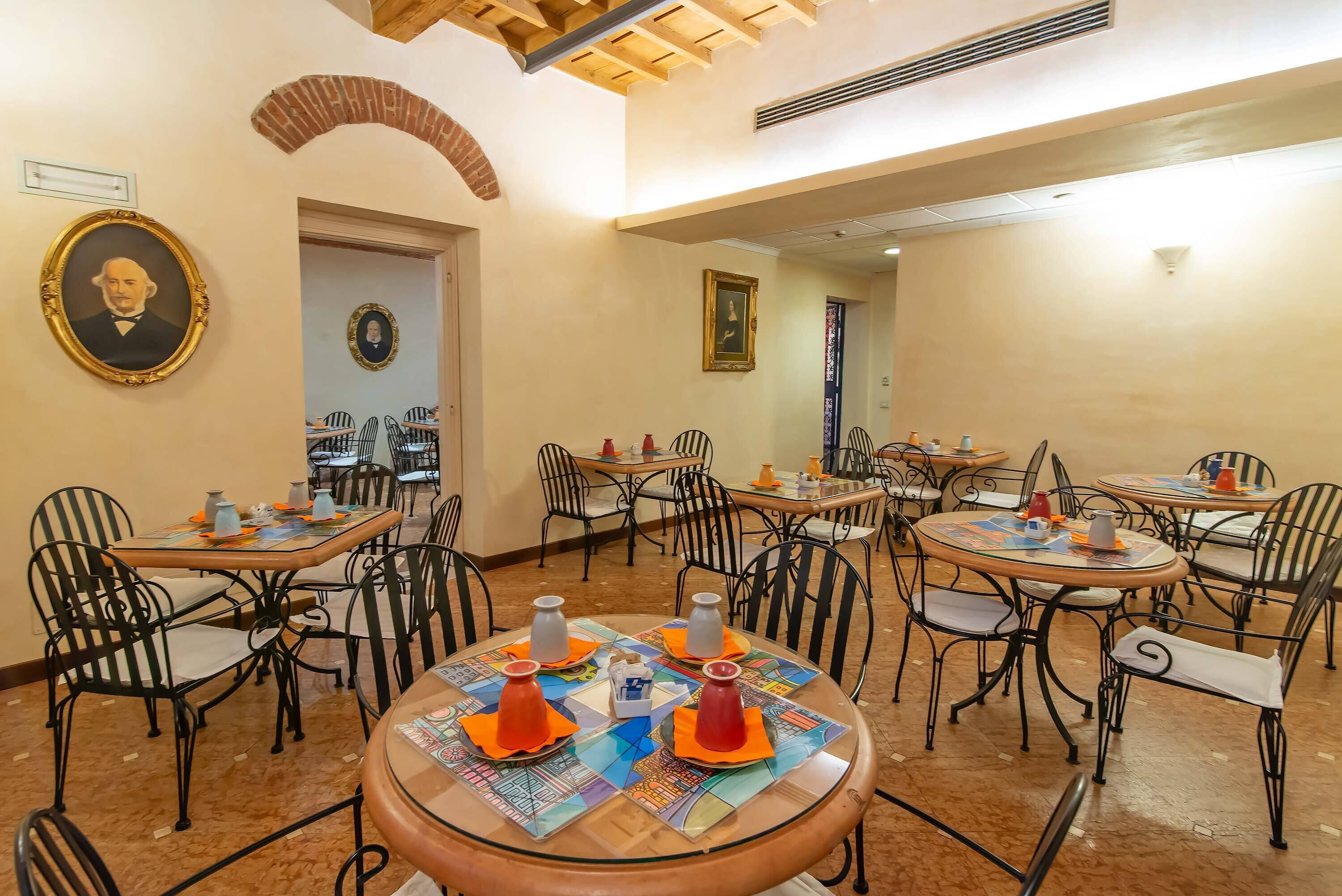 A dining area with round tables, black metal chairs, and orange napkins.