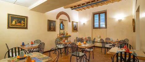 Un comedor con varias mesas y sillas, con piso de baldosas y vigas de madera en el techo.