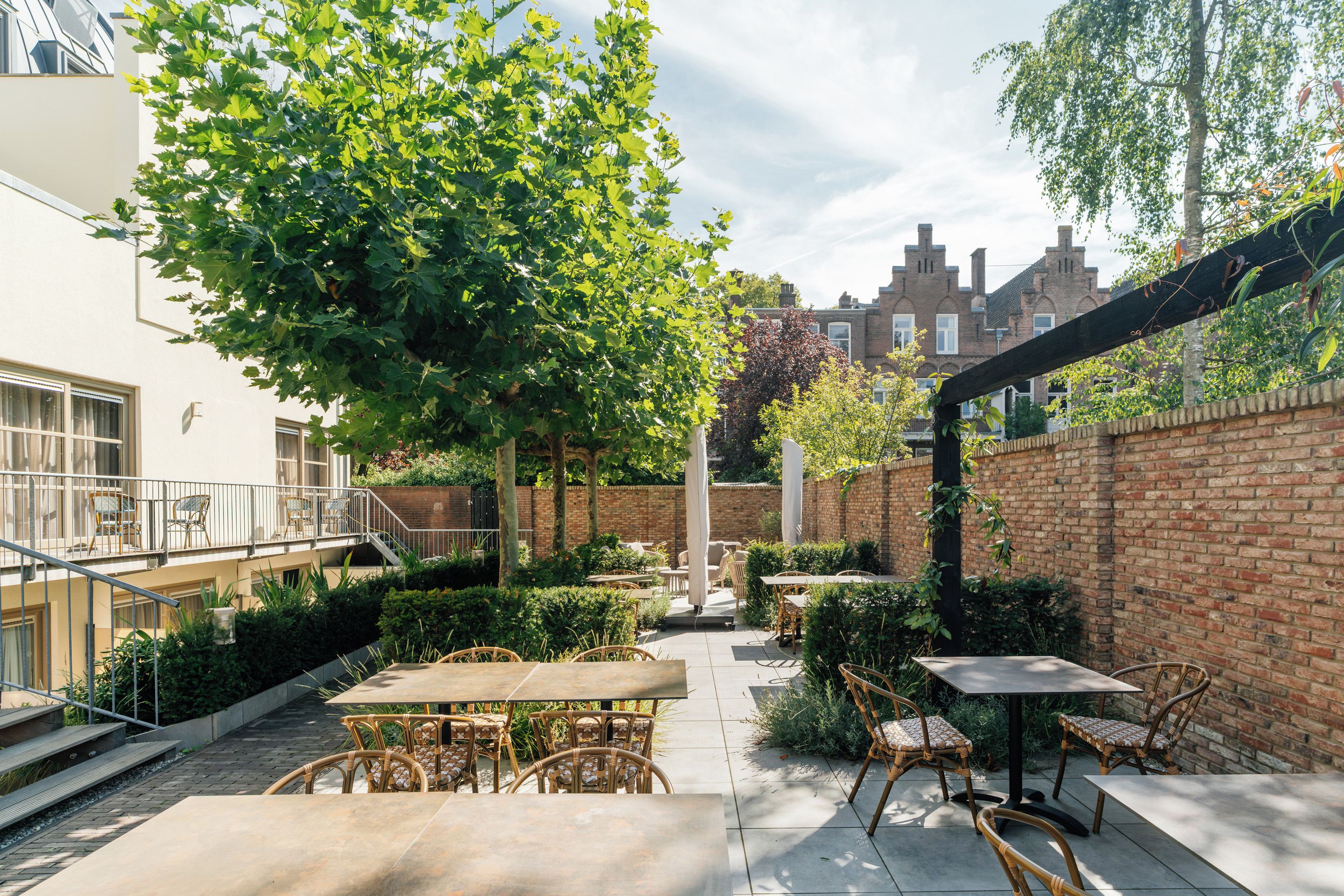 An outdoor patio area with tables and chairs, surrounded by greenery and brick walls.