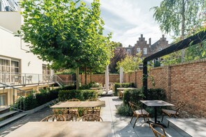 An outdoor patio area with tables and chairs, surrounded by greenery and brick walls. - Malie House Utrecht (Utrecht)