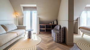 A modern loft bedroom with a high ceiling, a built-in wooden cabinet, a patterned armchair, and a large window with sheer curtains. - Malie House Utrecht (Utrecht)